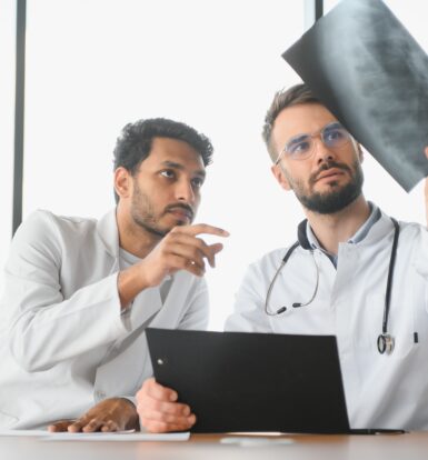 doctors reviewing an X-ray and discussing prior authorization requirements for Isoniazid Sulfate sublingual tablets for tuberculosis treatment under Caremark.