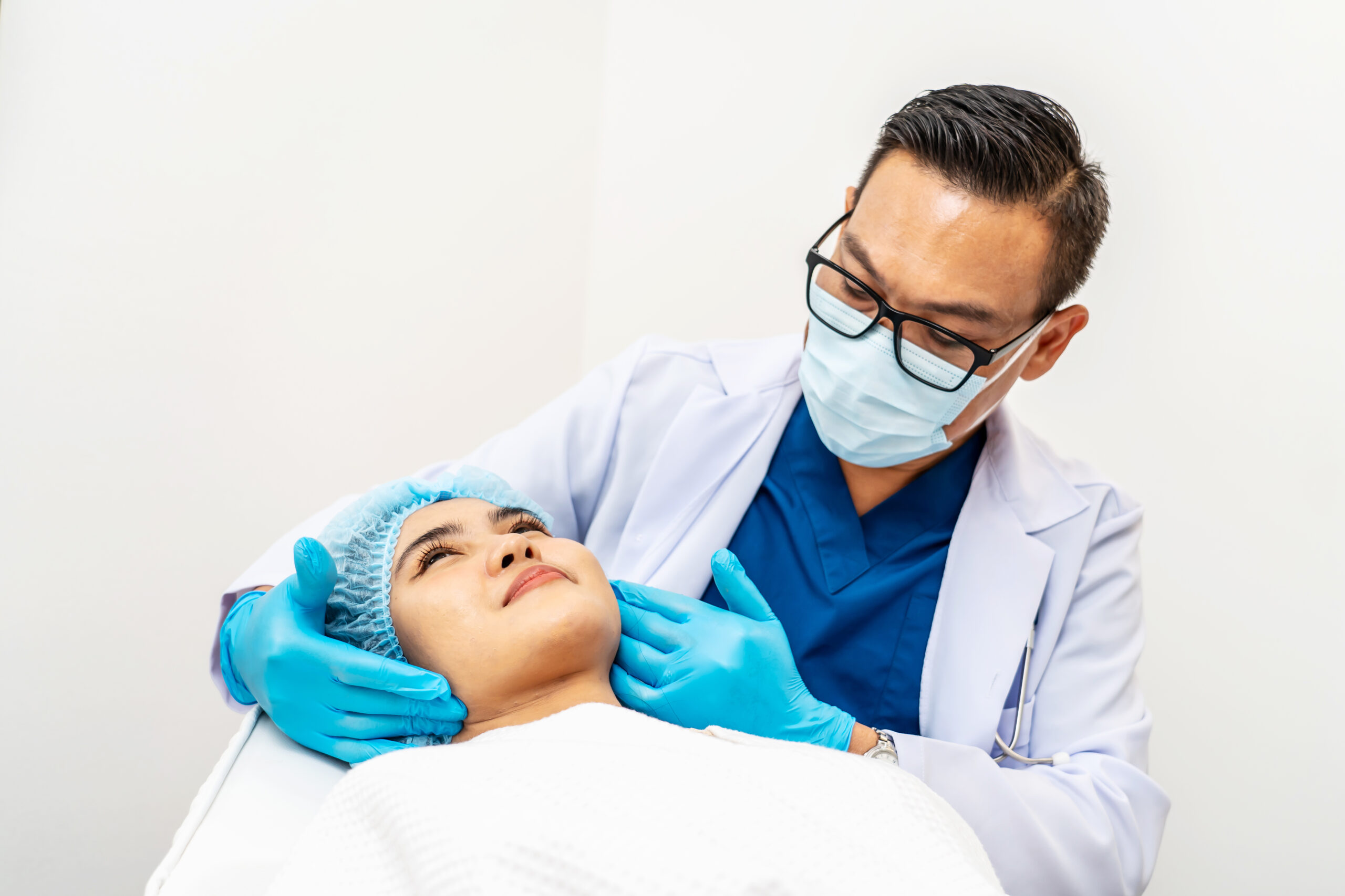 Doctor examining a patient's face with care while wearing medical gloves, mask, and a white coat in a clinical setting