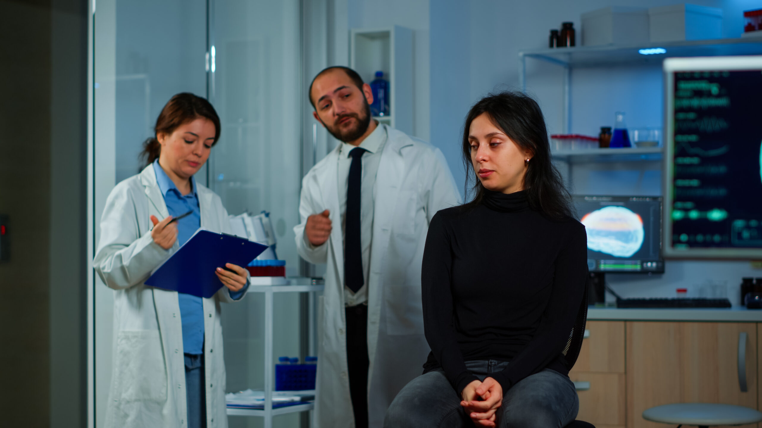 Patient sitting in a clinic with two healthcare professionals reviewing her case, one taking notes and the other explaining the treatment options.