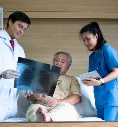 Doctor and nurse showing a chest X-ray to a patient with tuberculosis in a hospital bed, discussing treatment options.