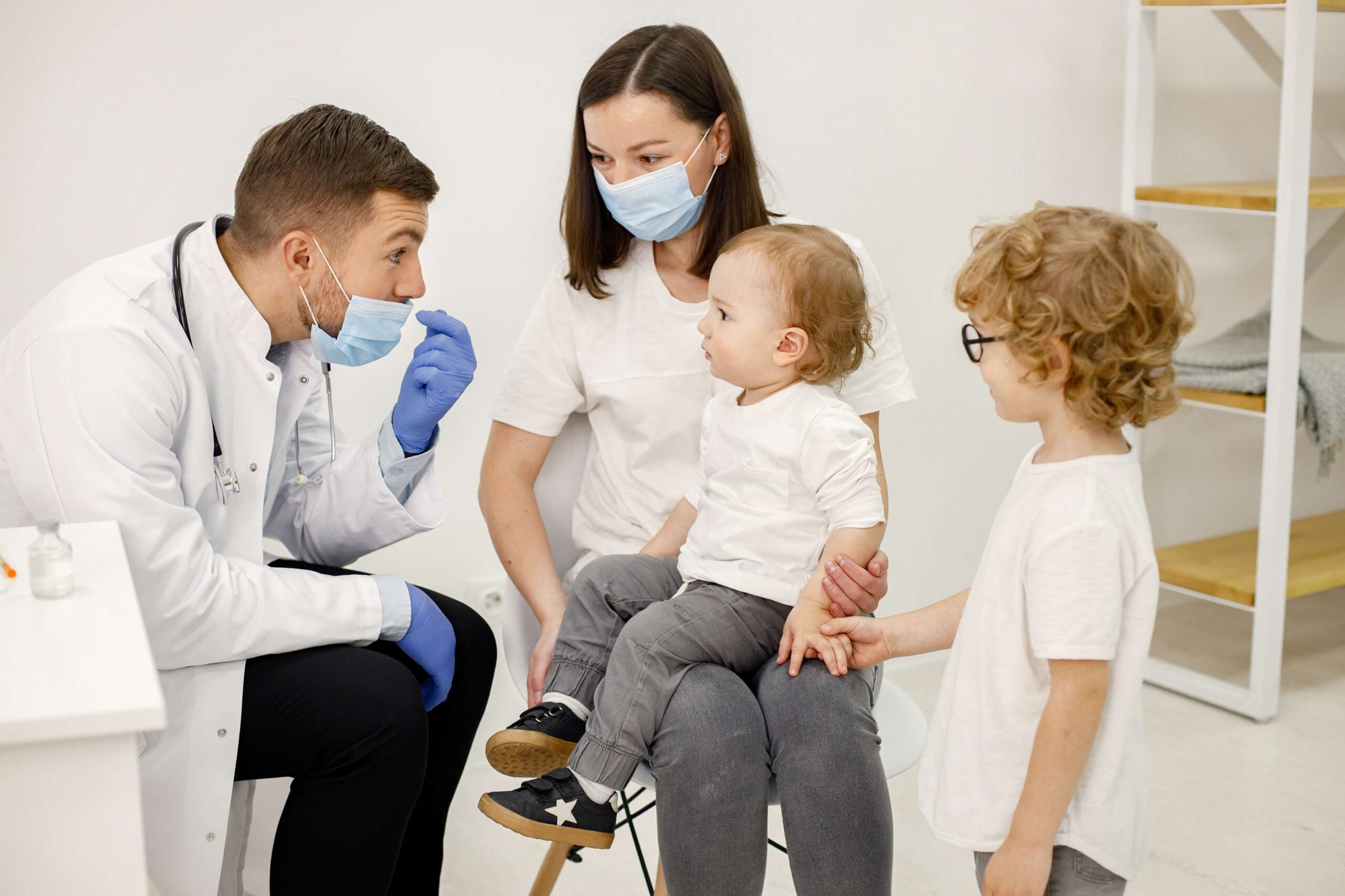 A healthcare provider interacting with a mother and two young children in a clinical setting, highlighting a supportive and family-friendly healthcare environment. The provider is engaged in explaining treatment options, fostering trust and communication with the patients.