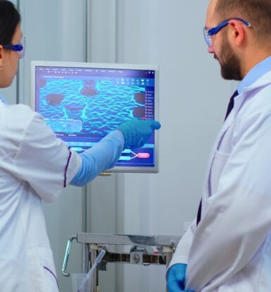 Two healthcare professionals in lab coats analyzing data on a computer screen, discussing medical coding and analytics