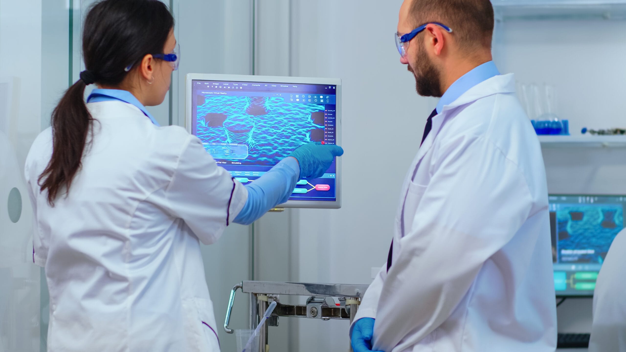 Two healthcare professionals in lab coats analyzing data on a computer screen, discussing medical coding and analytics