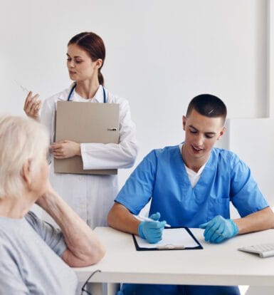 A healthcare professional verifying patient insurance details on a computer with documents and an insurance card on the desk.