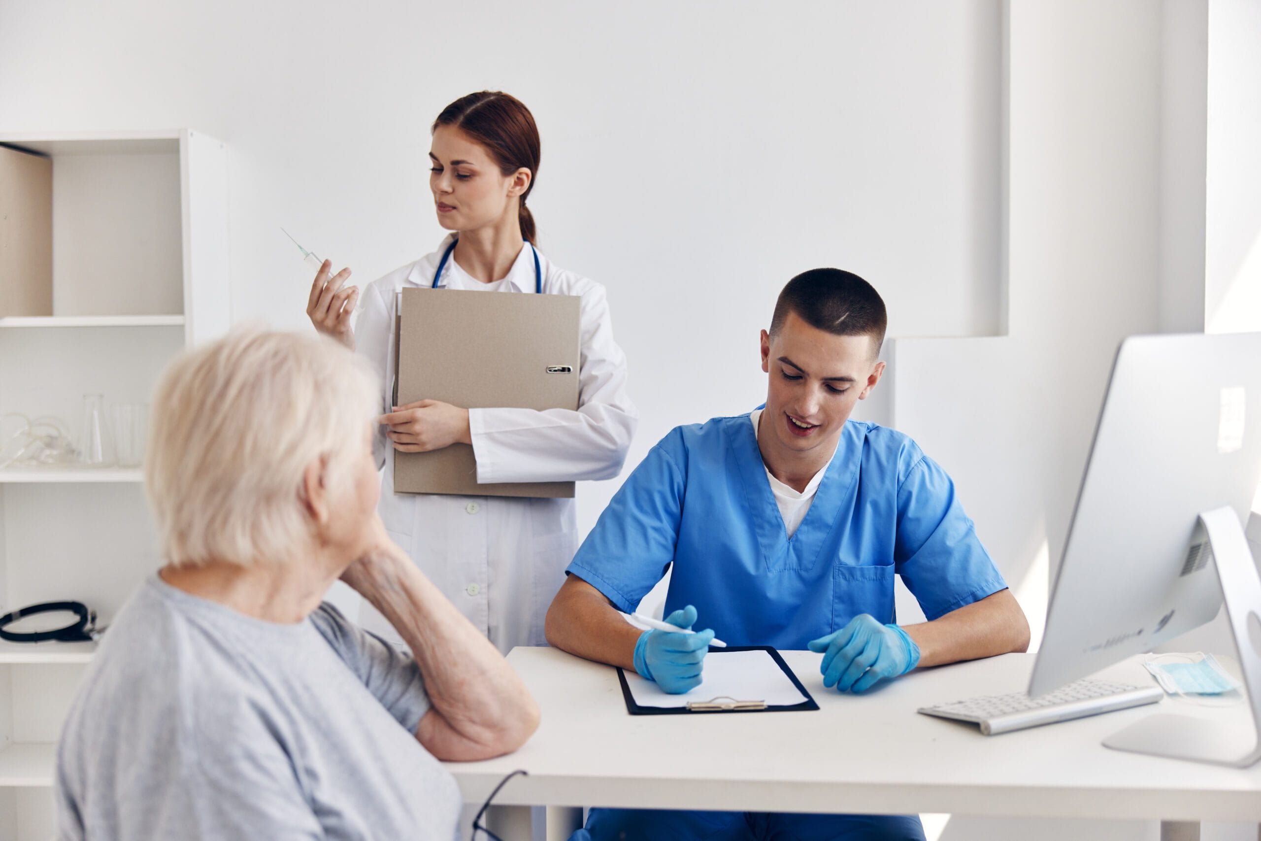 A healthcare professional verifying patient insurance details on a computer with documents and an insurance card on the desk.