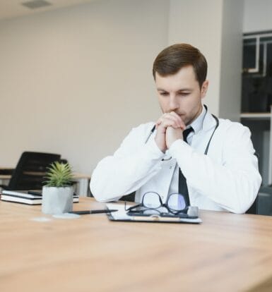 A physician smiling while consulting with a patient, supported by a virtual medical scribe.