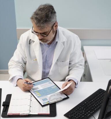 A healthcare provider reviewing documents at their desk, with a computer, a printed report, and a planner, symbolizing the prior authorization process in a medical setting.