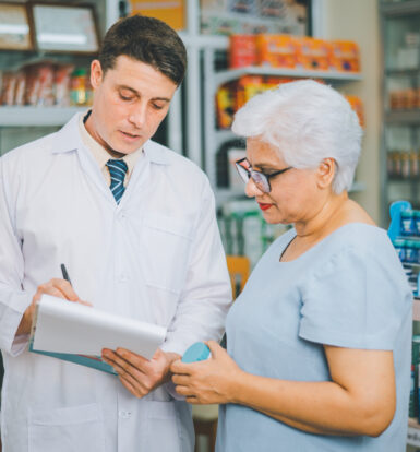 A pharmacist discussing medication with an elderly woman in a pharmacy setting, representing personalized care and billing accuracy.