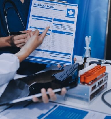 Healthcare professionals reviewing a medical form with lab samples and medical tools on a desk, symbolizing accuracy and efficiency in medical coding.