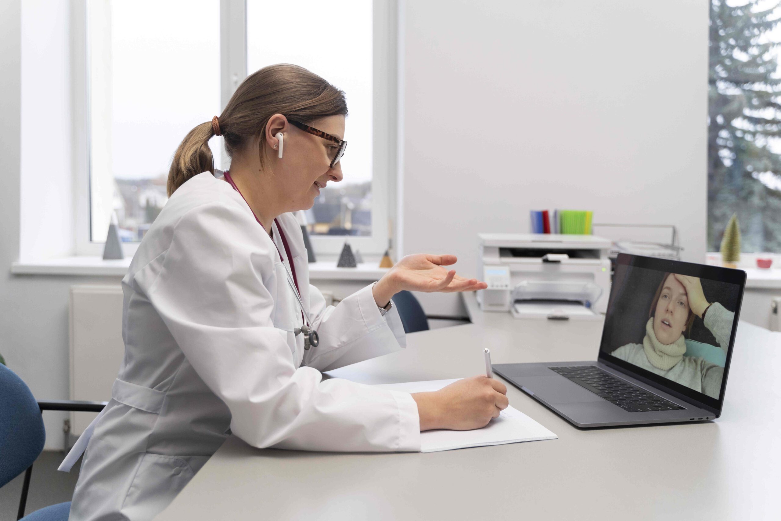 A doctor in a white coat conducting a virtual consultation with a patient on a laptop, representing telemedicine and patient engagement supported by virtual medical receptionists