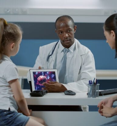 A doctor showing a digital image of a virus to a young patient and her mother, highlighting the use of medical technology in care.