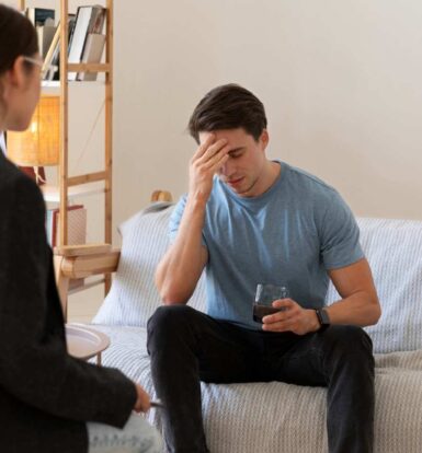 A distressed man holding a glass of water while discussing with a therapist, representing challenges in prior authorization for Invega Sustenna.