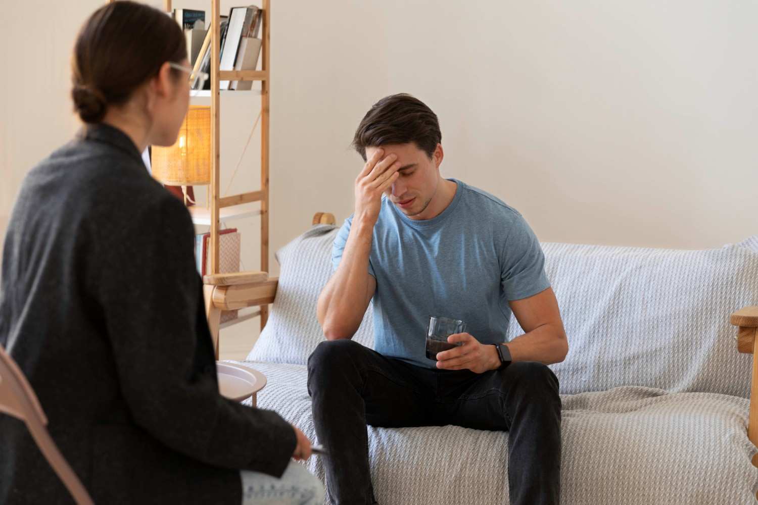 A distressed man holding a glass of water while discussing with a therapist, representing challenges in prior authorization for Invega Sustenna.