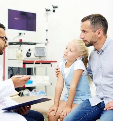 A doctor explaining the prior authorization process to a concerned father and his young daughter in a clinic setting.