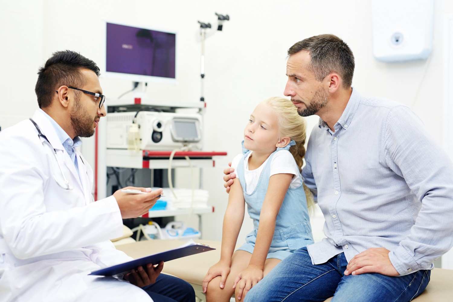 A doctor explaining the prior authorization process to a concerned father and his young daughter in a clinic setting.