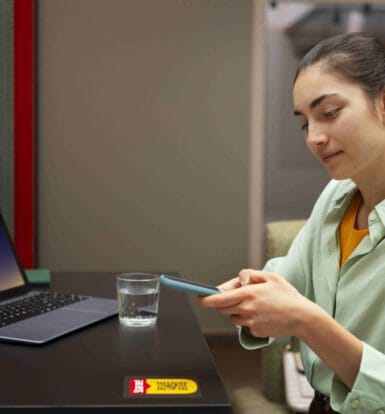 A healthcare professional using a smartphone and laptop to manage telemedicine outsourcing tasks efficiently.