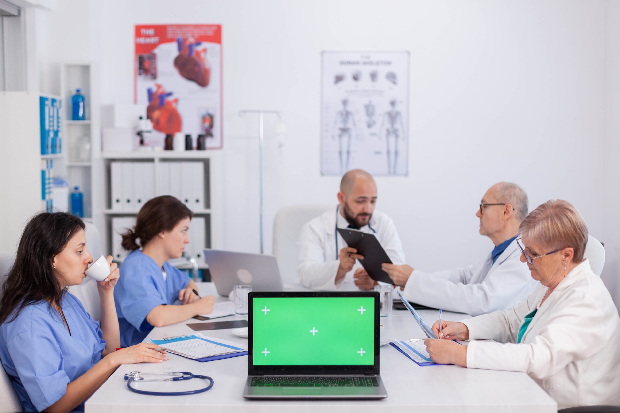 A team of doctors and nurses in a collaborative meeting, reviewing patient files and discussing medical strategies, with a laptop at the center symbolizing telemedicine support.