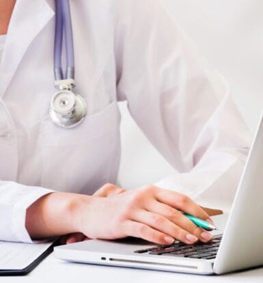 Doctor using a laptop to manage medical billing and coding tasks, showcasing a streamlined workflow.