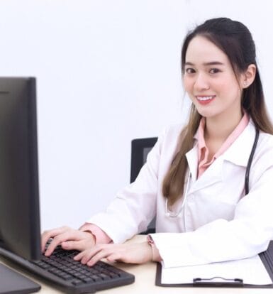 A smiling healthcare professional working on a computer, symbolizing the efficiency of outsourcing virtual medical assistants for administrative tasks.