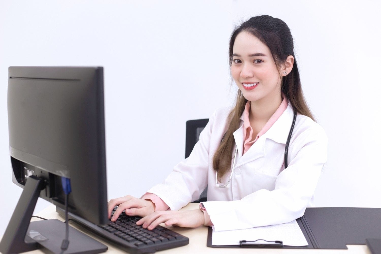 A smiling healthcare professional working on a computer, symbolizing the efficiency of outsourcing virtual medical assistants for administrative tasks.