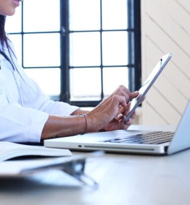 A healthcare professional using a tablet and laptop for telemedicine coordination, symbolizing the role of Virtual Medical Assistants.