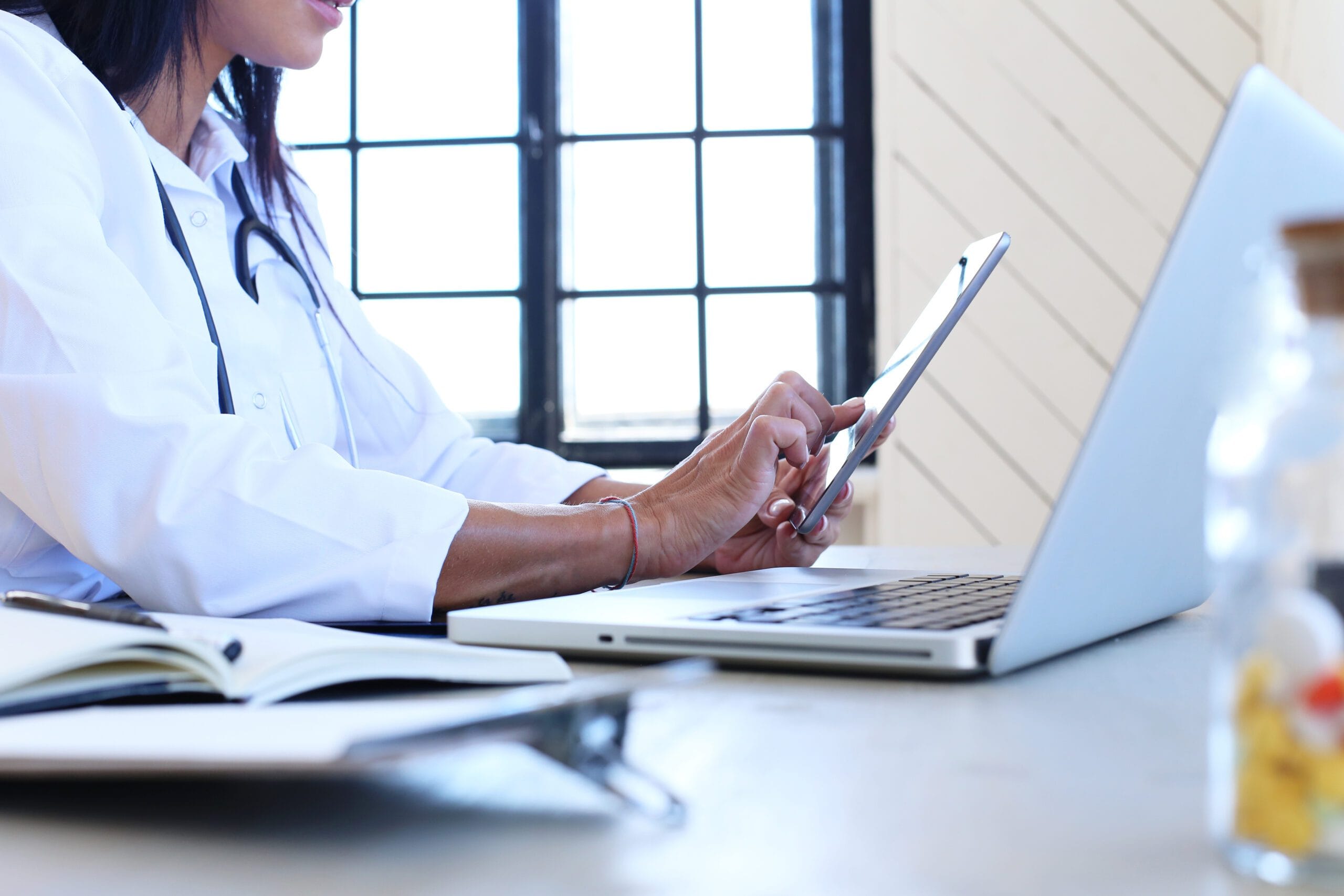 A healthcare professional using a tablet and laptop for telemedicine coordination, symbolizing the role of Virtual Medical Assistants.