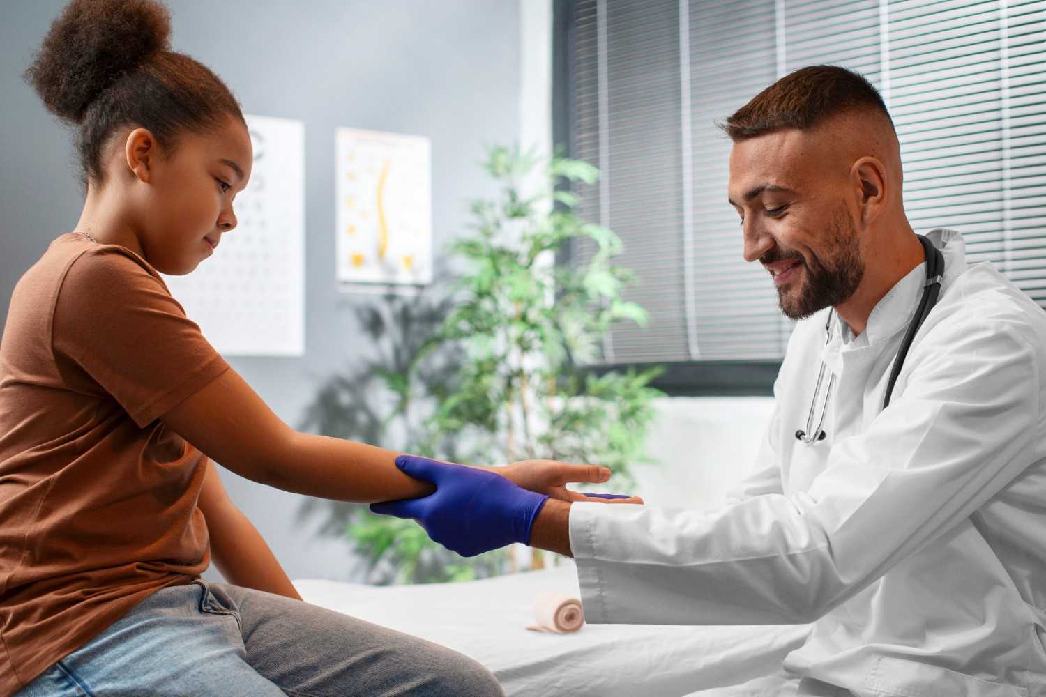 A doctor in a white coat and gloves is gently examining a young girl’s arm, smiling as they interact. The setting is a bright medical office with plants and a calm environment.