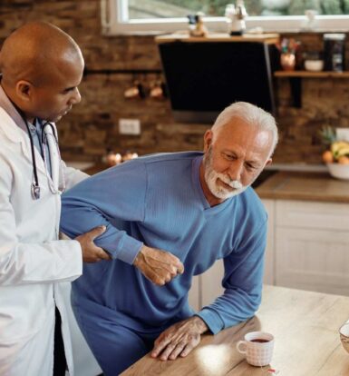 A doctor assisting an elderly male patient in a home setting during a medical consultation.