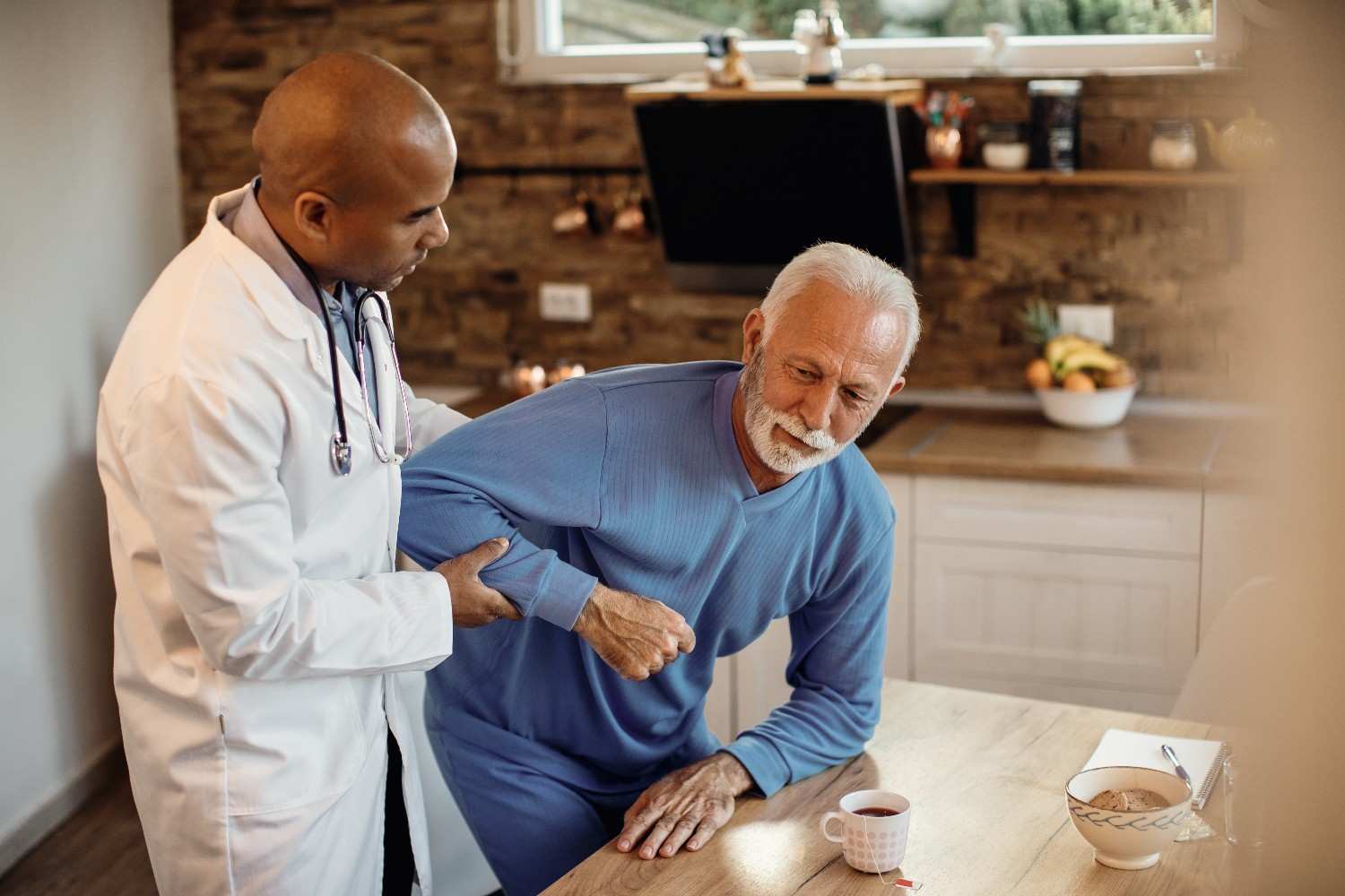 A doctor assisting an elderly male patient in a home setting during a medical consultation.