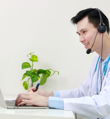 Virtual Medical Assistant in a white coat with a headset working on a laptop, remotely supporting a healthcare practice.