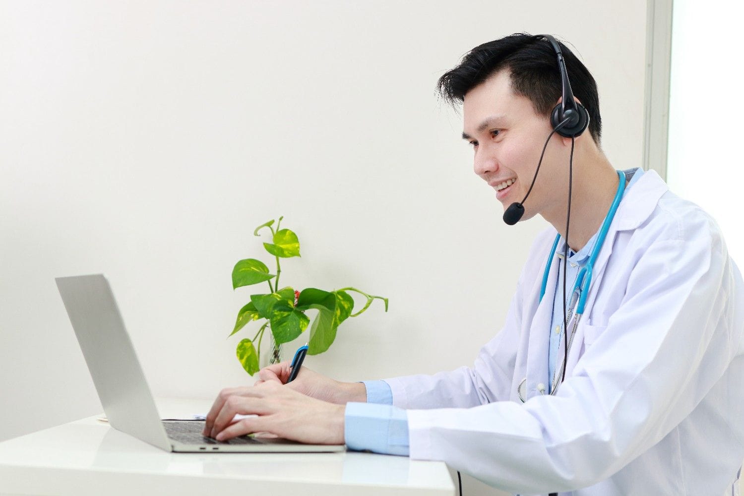 Virtual Medical Assistant in a white coat with a headset working on a laptop, remotely supporting a healthcare practice.