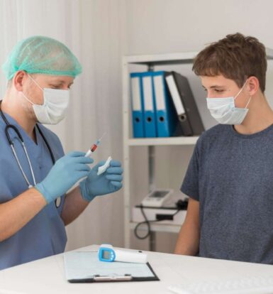 A healthcare professional in scrubs and a mask preparing an injection while consulting with a patient wearing a mask, highlighting a prior authorization process in healthcare.