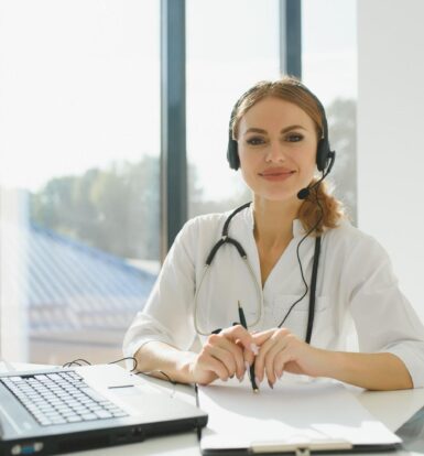 Female healthcare professional with a headset sitting at a desk with a laptop, ready to assist as a Virtual Medical Assistant.