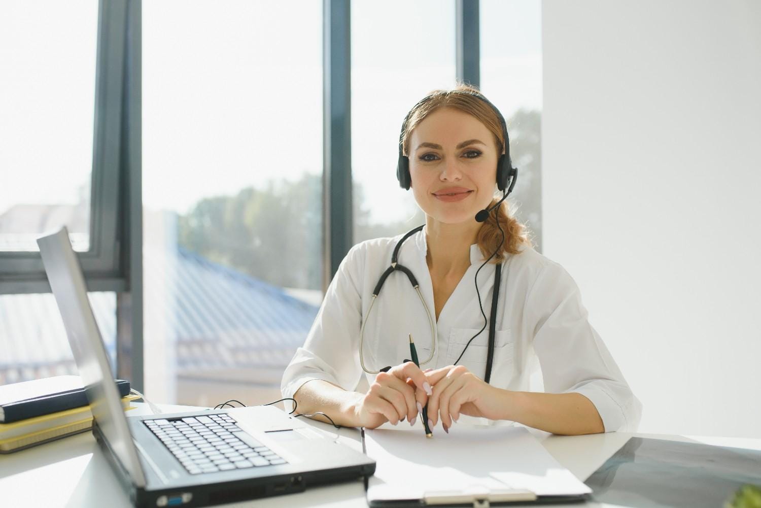 Female healthcare professional with a headset sitting at a desk with a laptop, ready to assist as a Virtual Medical Assistant.