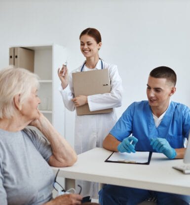 Healthcare providers discussing a patient's care plan, with a nurse and doctor smiling and reviewing documents with an elderly woman.