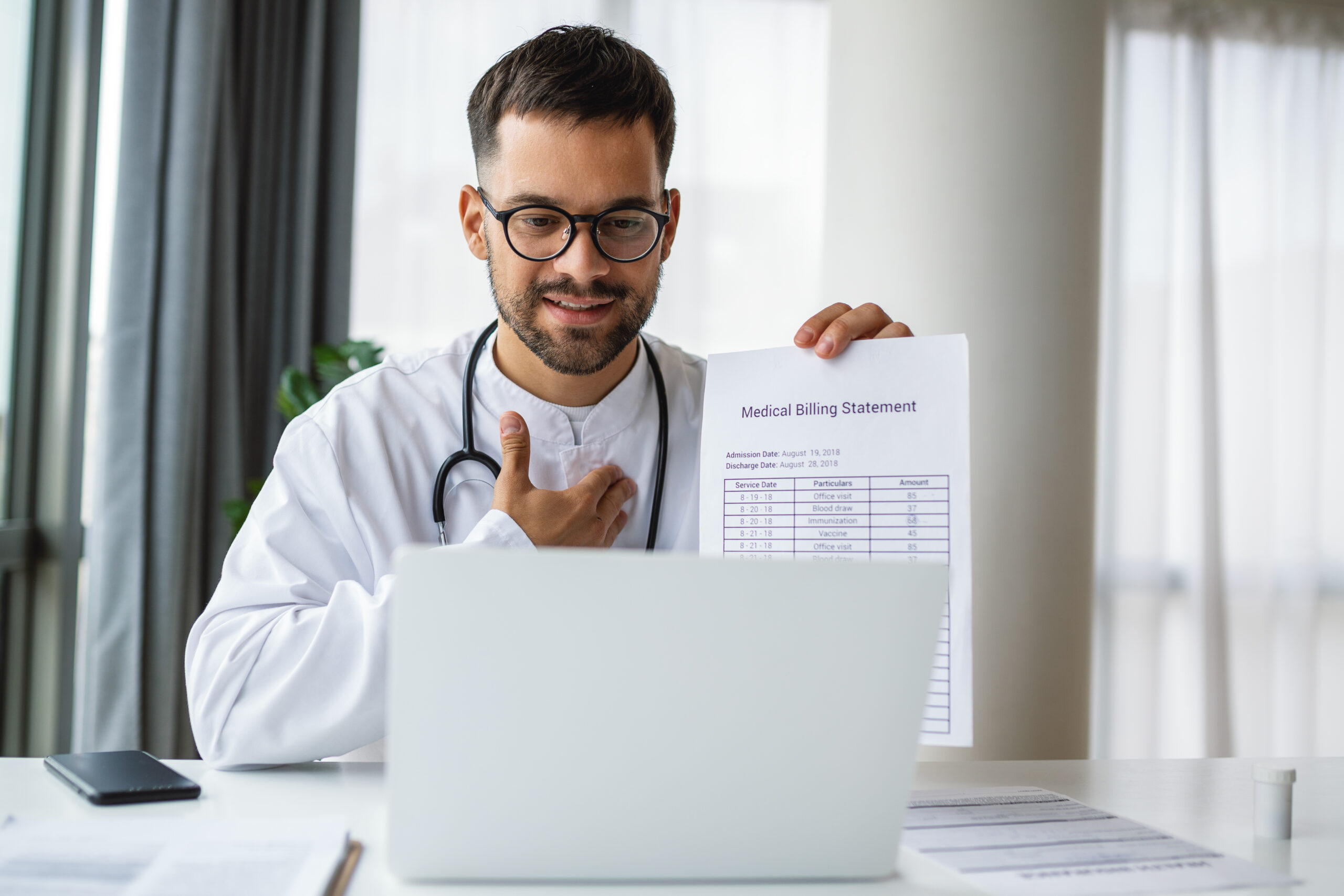 Doctor holding a medical billing statement while working on a laptop, symbolizing outsourced billing and HIPAA-compliant practices.