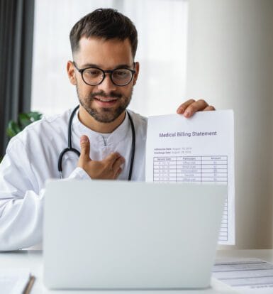 A doctor holding a medical billing statement while sitting at a desk with a laptop, explaining billing details during a virtual consultation.