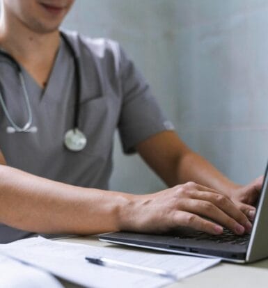 A healthcare professional in scrubs working on a laptop to manage insurance workflows and administrative tasks.