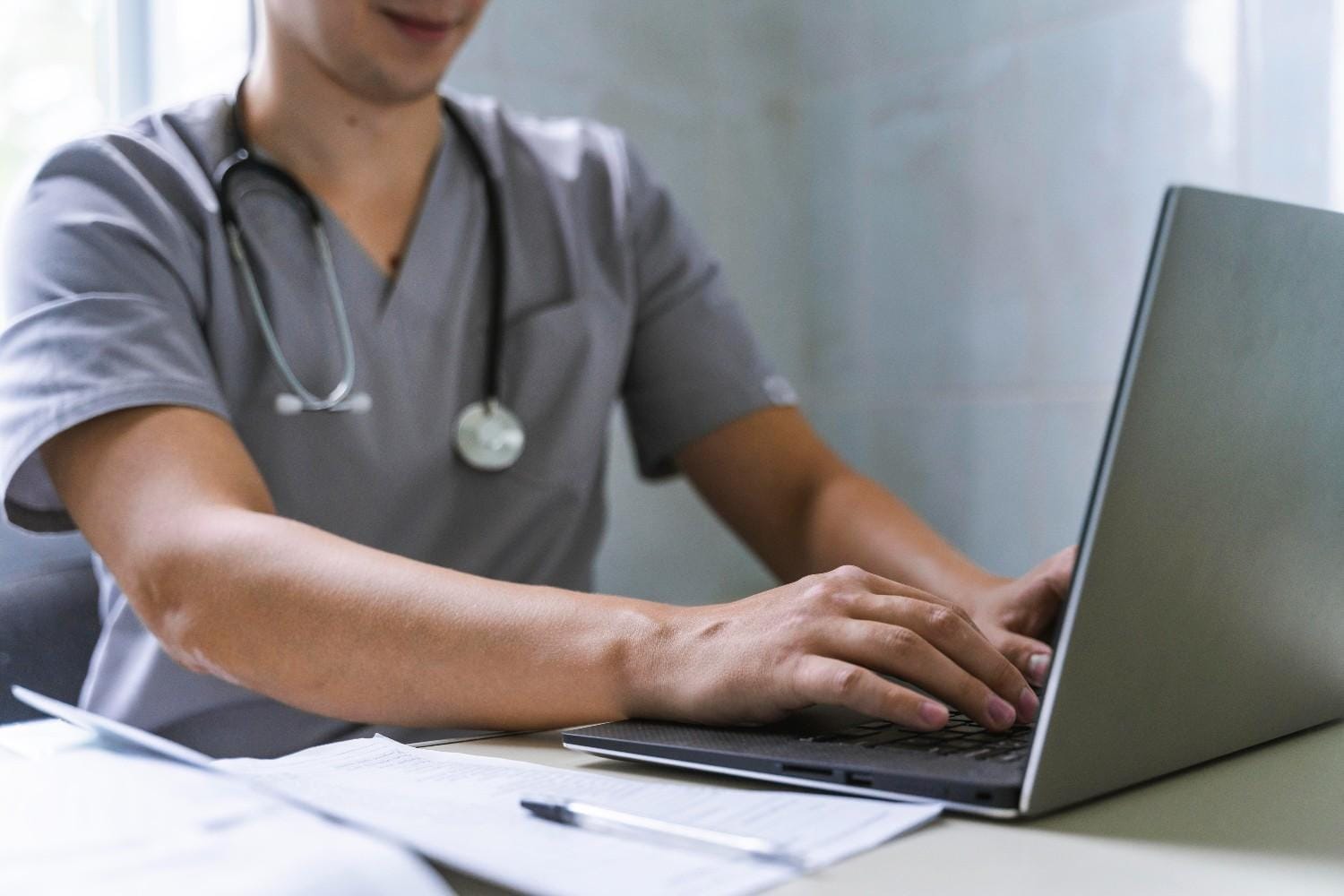 A healthcare professional in scrubs working on a laptop to manage insurance workflows and administrative tasks.