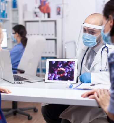 Doctor showing a digital image of a virus to a young patient and her mother, representing patient education and virtual support in healthcare.