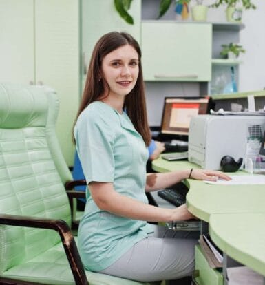 Virtual medical assistant working remotely at a desk, managing patient scheduling and administrative tasks on a computer.