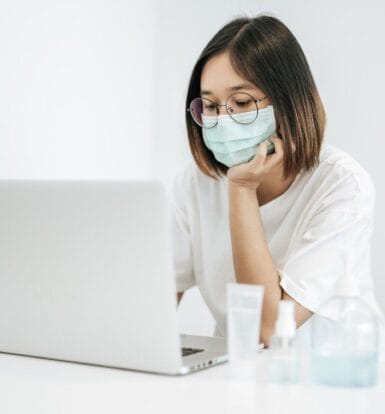 A healthcare professional wearing a mask and working on a laptop, showcasing secure and efficient virtual communication in healthcare.