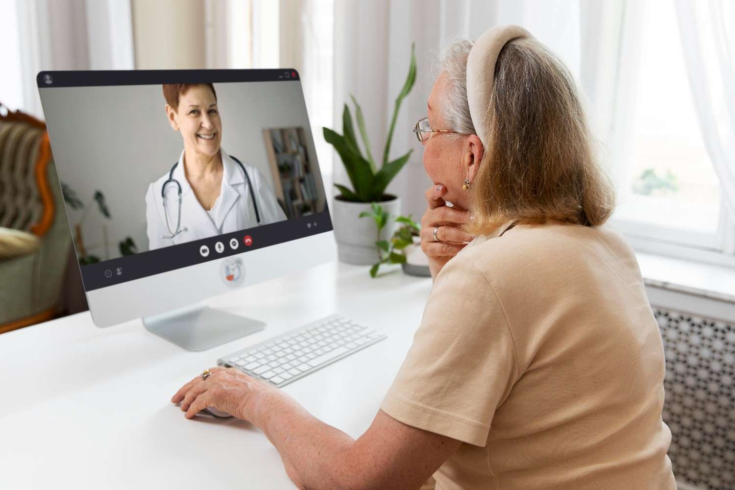 Elderly woman engaging in a telehealth appointment with a virtual medical receptionist on her desktop computer, showcasing efficient remote healthcare solutions.