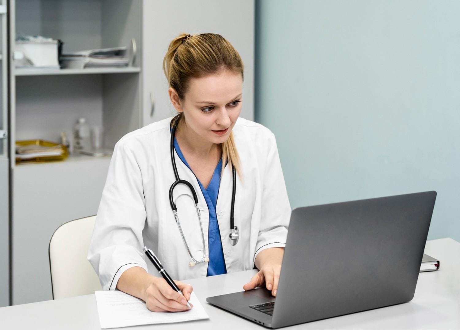 Doctor wearing a stethoscope, working on a laptop while taking notes, demonstrating secure handling of patient information.