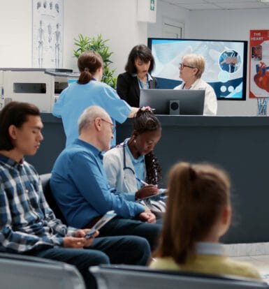 A busy hospital waiting area with patients seated, nurses reviewing files, and administrators working at the reception desk, symbolizing the role of telemedicine outsourcing in improving patient care and operational efficiency.