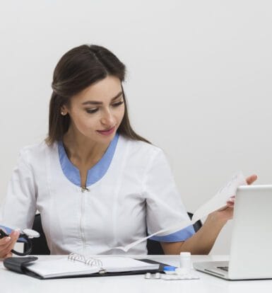 Female healthcare provider reviewing medical reports and using a laptop for LTC pharmacy billing tasks.