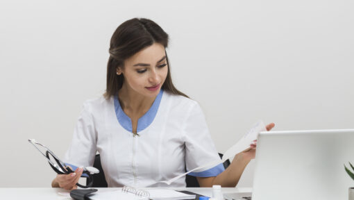 Female healthcare provider reviewing medical reports and using a laptop for LTC pharmacy billing tasks.