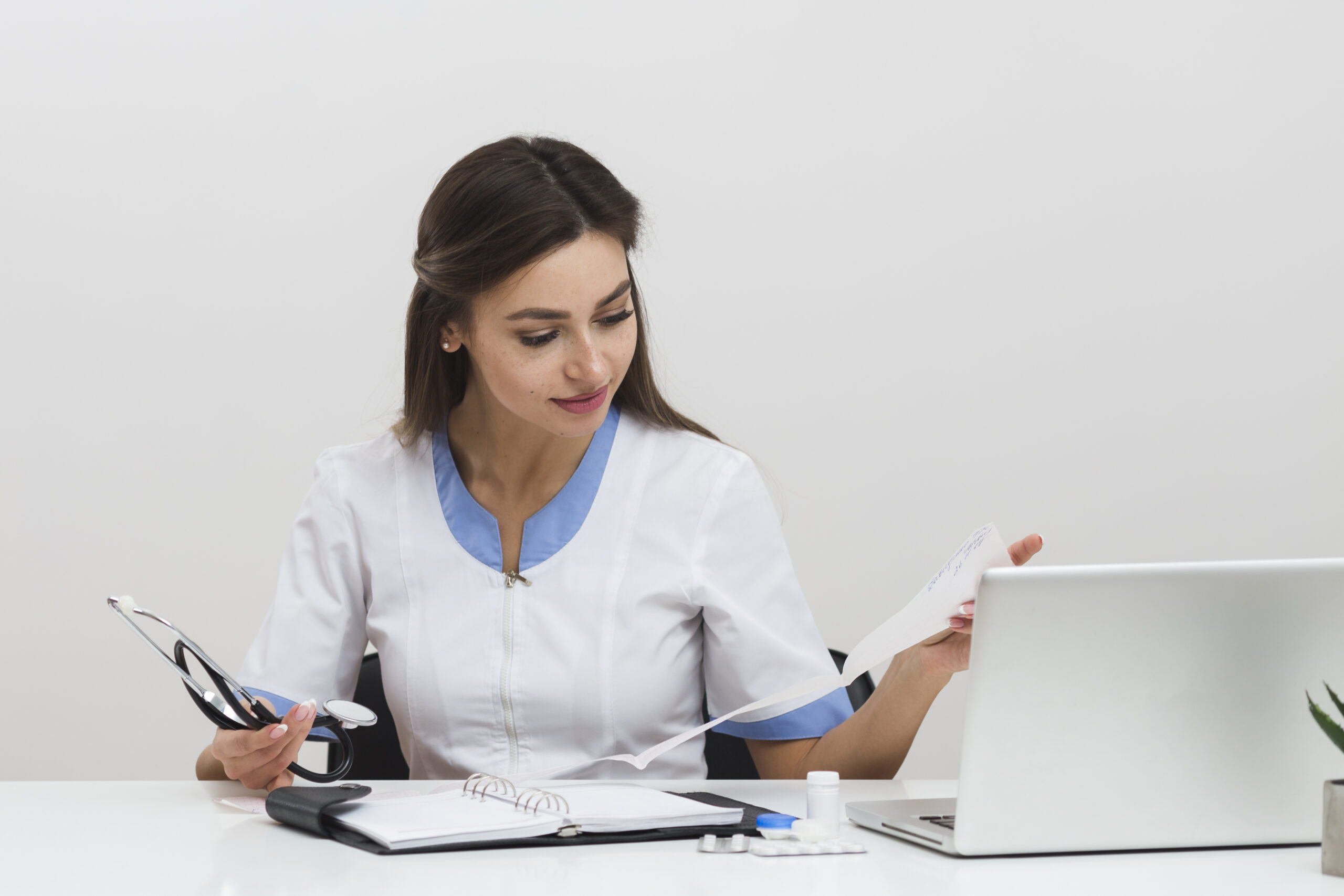 Female healthcare provider reviewing medical reports and using a laptop for LTC pharmacy billing tasks.