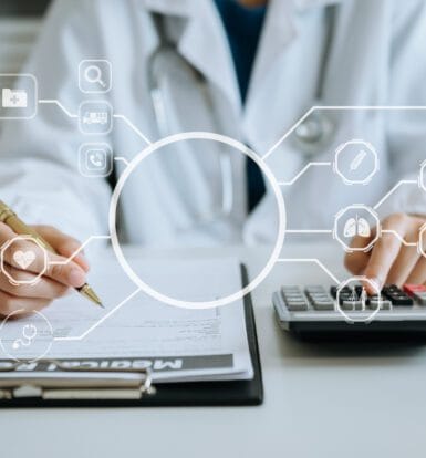 Healthcare worker analyzing medical coding data on a laptop screen with charts and claim forms visible.