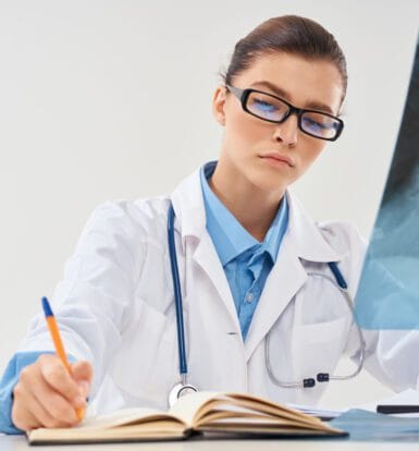 Medical coder working on a laptop, surrounded by healthcare documents and coding software.